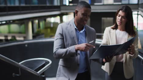 Diverse-businessman-and-businesswoman-talking-and-talking-up-stairs-of-modern-office