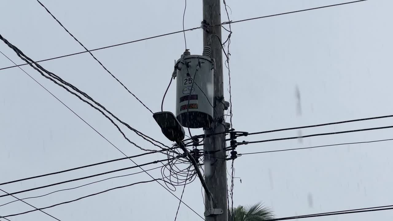 Electric transformer on a concrete utility pole during rainfall. Ideal for weather, energy, infrastructure, and urban environment editorial content