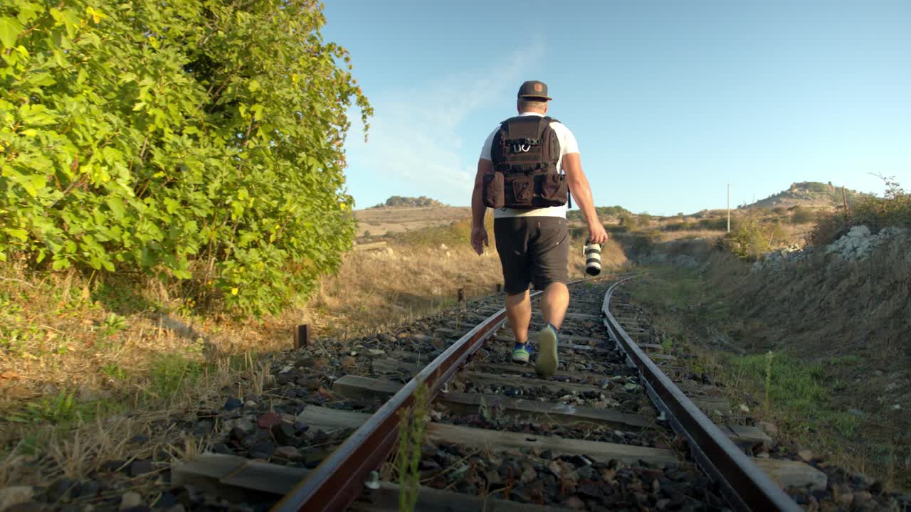 un fotógrafo masculino caminando por vías de tren desiertas con una sensación veraniega