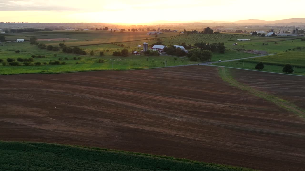 Drone wide shot of idyllic and picturesque rural landscape at golden sunset. American countryside with driving car on intersection road. Peaceful morning in United States