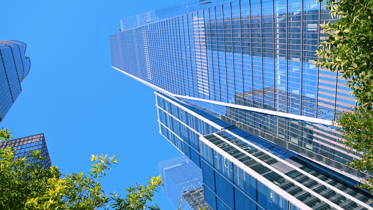 Modern glass buildings of New York reflecting beautiful blue clear sky. Low angle view at the high-rises walking by the streets of metropolis