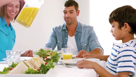 Nette-Familie-Beim-Mittagessen-Und-Mutter-Gießt-Orangensaft-Ein