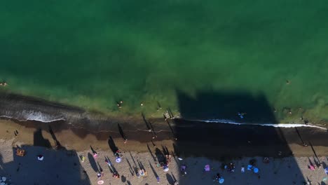 Drone-shot-flying-over-a-crowded-beach-and-out-to-sea