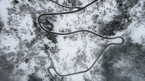 Lowering-aerial-pedestal-approaching-mountain-road-surrounded-by-snow