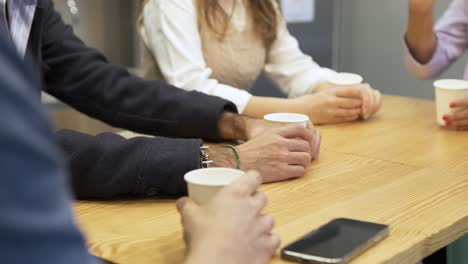 business people's hands holding disposable glasses at table in canteen