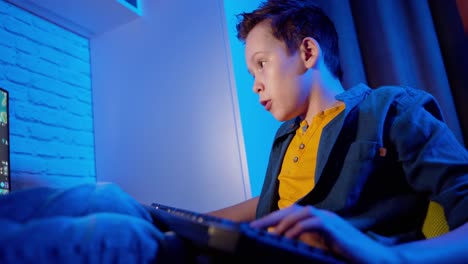 excited boy playing and winning in online video game. teenager sitting comfortably at home and playing on his personal computer. blue light in the room.