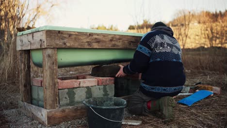 the man is securing the large rock onto the stove beneath the diy hot tub - static shot
