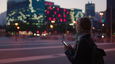 Porträt-Einer-Jungen-Blonden-Frau,-Die-Nachts-Mit-Der-Smartphone-Social-Media-App-In-Einer-Stadt-SMS-Surft-Und-Die-Lichter-Genießt