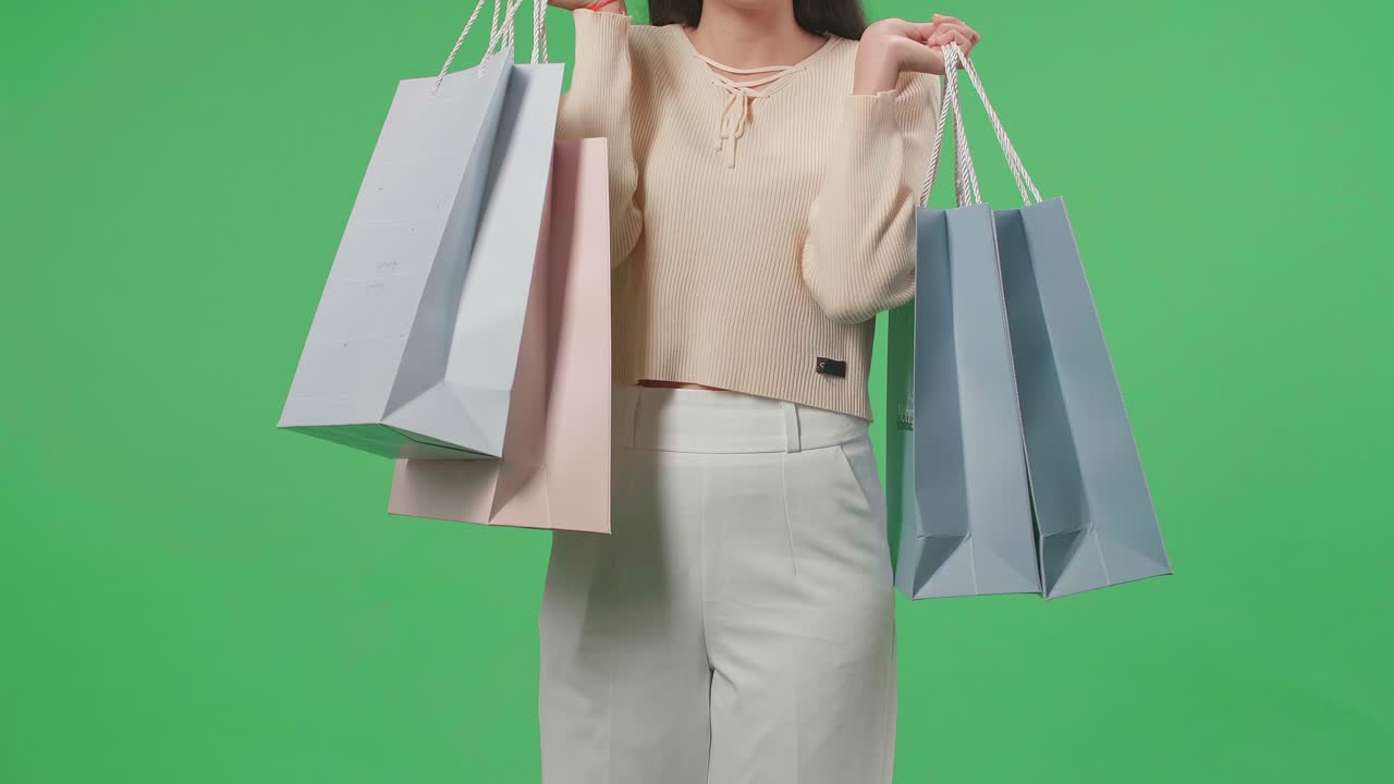 Front View Of A Shopping Woman Holding Shopping Bags Up Before Posing And Smiling To Camera While Standing In Front Of Green Screen