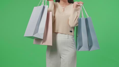 front view of a shopping woman holding shopping bags up before posing and smiling to camera while standing in front of green screen