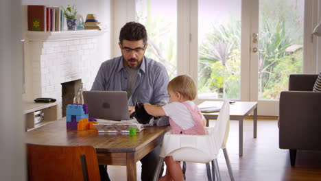 father working from home on laptop as son plays with toys