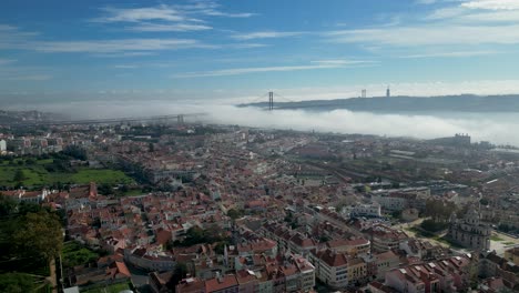 Daytime-aerial-of-city-dwelling-residential-area,-water-surface-with-iconic-25-April-Bridge-emerges,-connecting-both-coast-with-its-graceful-arches