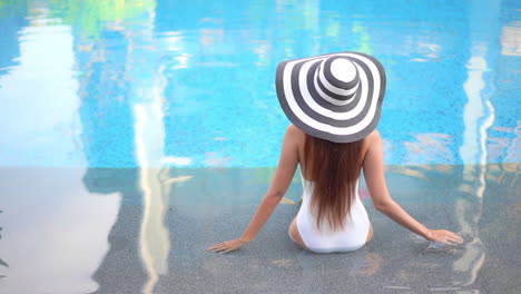 Back-View-of-Lonely-Slender-Woman-in-Swimsuit-and-Floppy-Hat-in-Shallow-Swimming-Pool-Water,-Fashion-Model-in-Tropical-Paradise,-Full-Frame