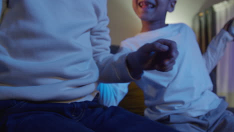 cerca de las manos de dos niños jóvenes en casa jugando con consola de juegos de computadora en la televisión sosteniendo controladores tarde en la noche 9