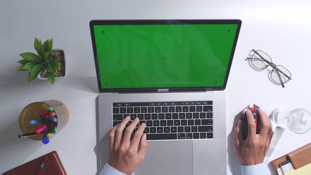vista de arriba hacia abajo de una computadora portátil con pantalla verde simulada pantalla chromakey en un escritorio de oficina de madera al lado de la libreta con bolígrafos, gafas y un vaso de agua.