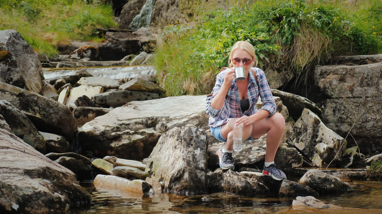 женщина пьет чистую воду, набранную из ручья норвежский водопад tvindefossen 4k видео