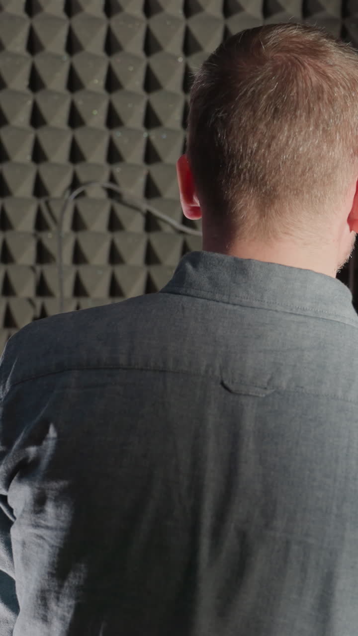 파란 셔츠를 입은 남자가  피아노를 연주하고, 그의 그림자가 검은색 음향 벽에 여있는 뒤쪽.