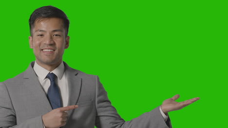 정장을 입고 웃는 사업가가 녹색 화면에 대해 무언가를 제시하거나 보여줍니다.