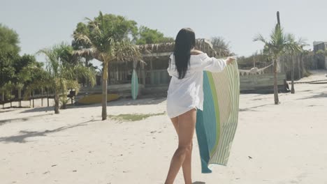 spaanse vrouw die handdoek legt op een zonnig strand, kopieer ruimte, langzame beweging.