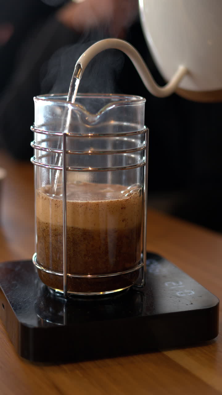 Close up of water pouring over coffee in a french press in a slow, circular motion. Vertical