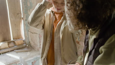 Close-Up-View-Of-A-Production-Worker-Helping-His-Female-Coworker-Read-A-Script-In-A-Ruined-Building