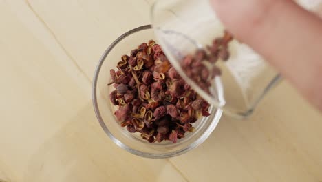 Dried-red-Sichuan-peppercorns-being-poured-into-a-glass-bowl-in-slow-motion