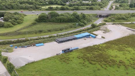 An-aerial-view-of-an-open-storage-yard-with-stacks-of-pipes,-located-near-a-highway-surrounded-by-greenery