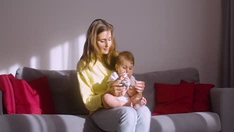 mujer sosteniendo a su hijo en su regazo mientras se sienta en el sofá de la sala de estar y juega con él con juguetes de animales