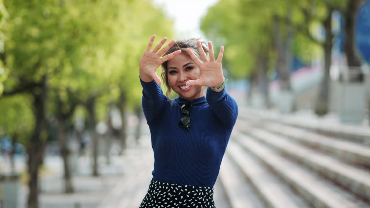 Donna con maglione e gonna blu seduta sui gradini, che si gode una giornata di sole in un parco urbano, mentre gioca con la macchina fotografica, circondata da alberi ed edifici moderni.