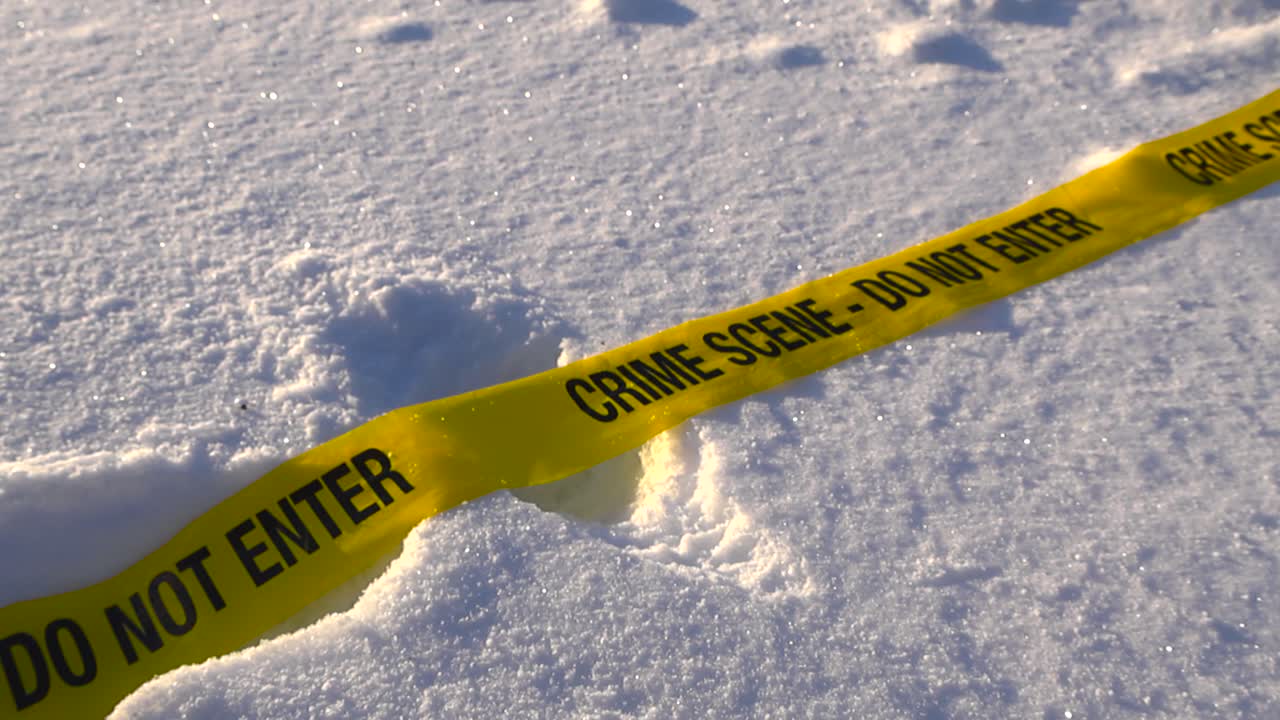 Low angle closeup of yellow crime scene tape fallen on snow covered landscape with boot prints and gentle wind, abandoned winter investigation scene. Cold trace on snowy terrain with shallow depth