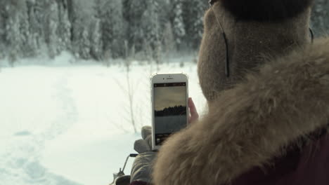 woman taking nature landscape photos with a smartphone in the winter time forest