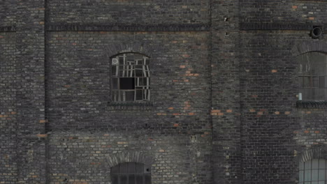 aerial shot as panning left, flying in front of a brick wall with huge windows that reflects a modern building