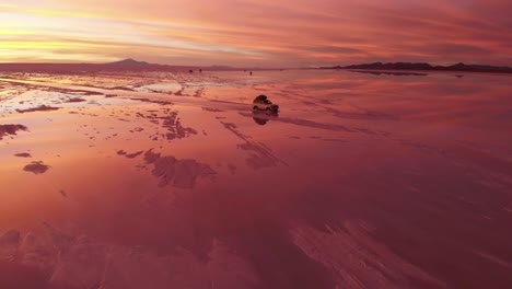 a jeep driving through salt flat in bolivia during a fiery sunset