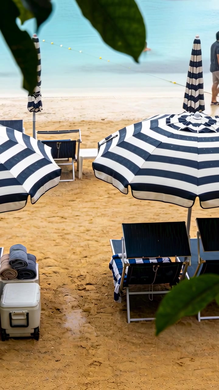Video verticale: Al mare, un papà con un bambino in braccio cammina sulla destra lungo la spiaggia, con ombrelloni e una boa.