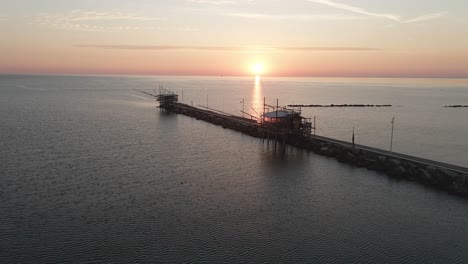 Vista-Aérea-Del-Paisaje-De-Una-Silueta-De-Trabucco,-Una-Máquina-De-Pesca-Tradicional,-En-La-Costa-Italiana,-Al-Atardecer