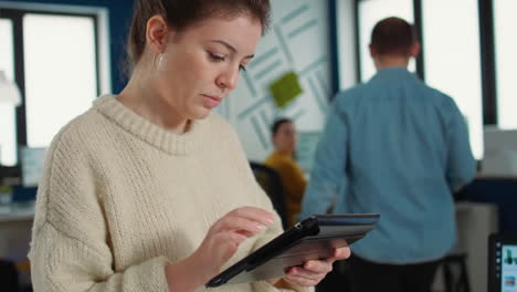 retrato de una mujer en una oficina de inicio recogiendo una tableta con gráficos de negocios e interactuando con una pantalla táctil