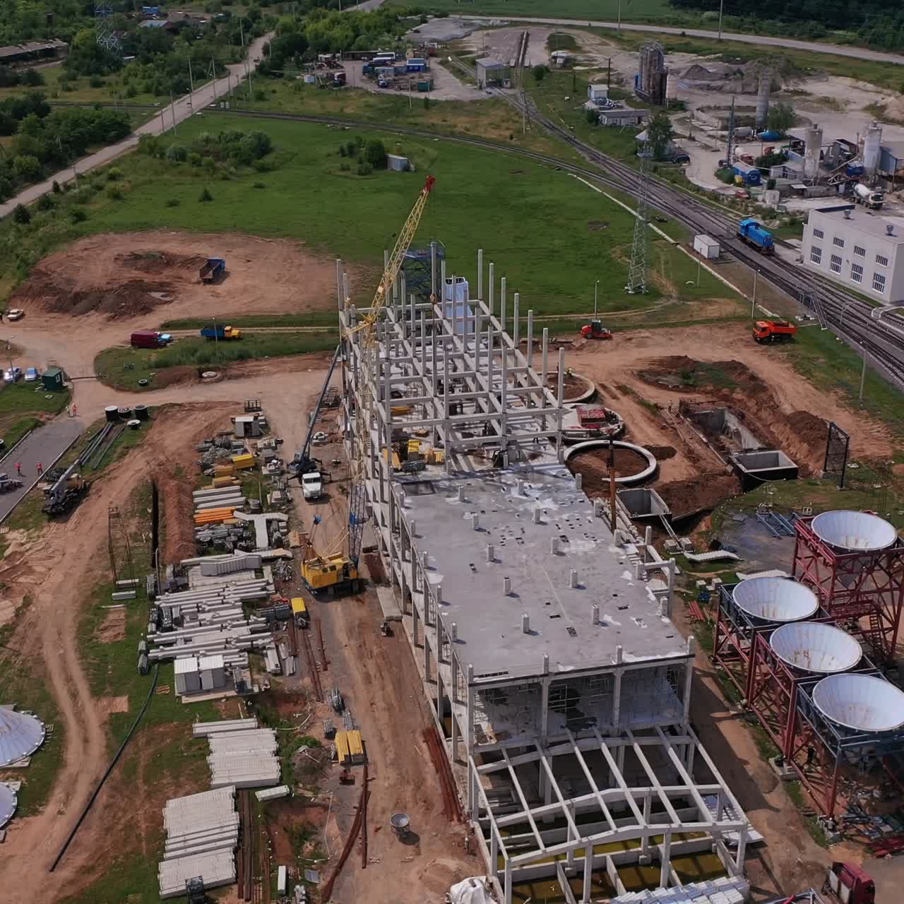 Construction area of the future granary complex. Building of a new modern grain elevator plant near the railways. Circle aerial view over the site