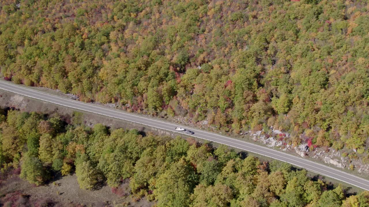 Dronebillede af motorvej, der skærer igennem farverige efterårstræer og en bil, Udbina, Kroatien