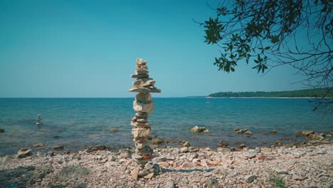 cinemagraph - bucle de vídeo sin fisuras de una torre de piedra gigante en una playa romántica en la costa mediterránea croata con una tabla de remo de pie inmóvil en el agua azul limpia y clara