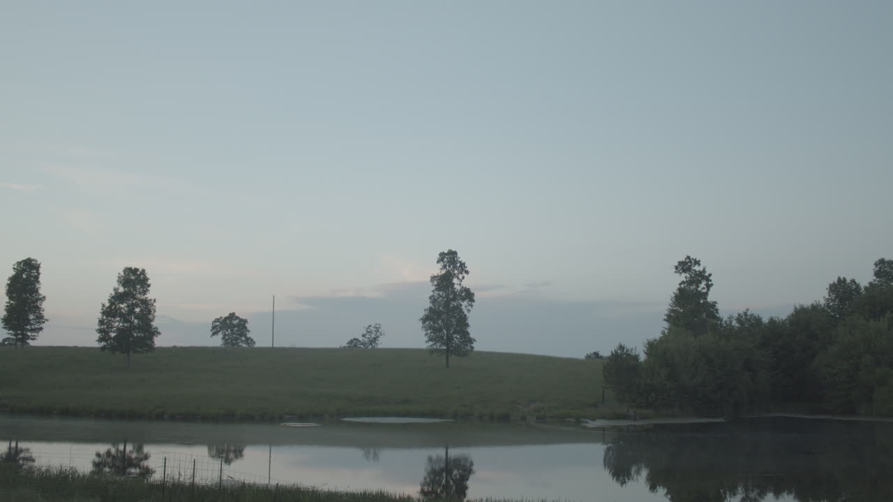 A tilt down from the blue sky reveals a dusky sunset near a country pond.