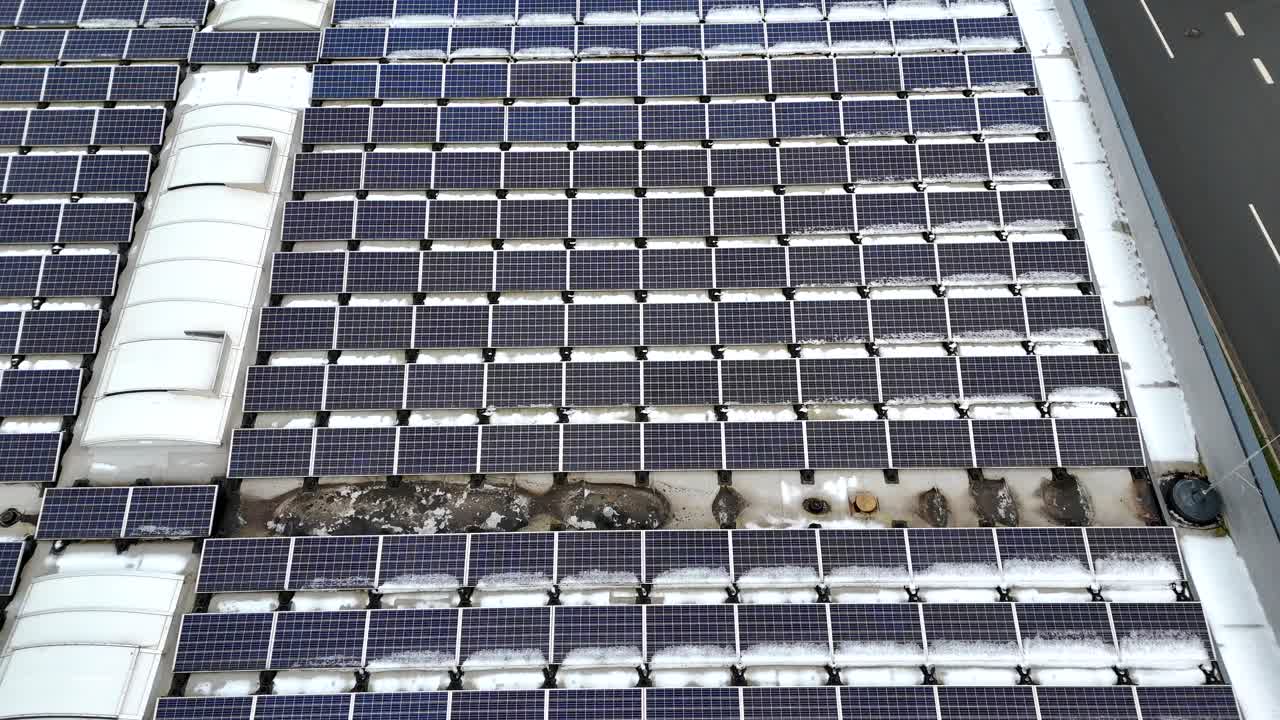 Solar panels on roof of warehouse during snowy winter day in USA. Low angle drone flyover. Production of green and renewable energy. Top down.