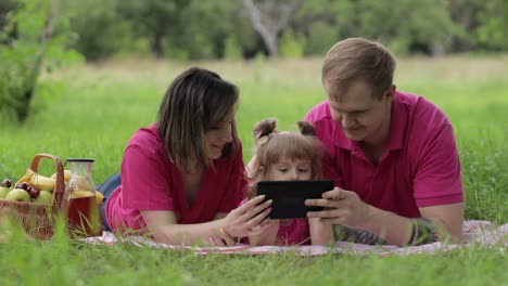 family weekend picnic. daughter child girl with mother and father play online games on tablet