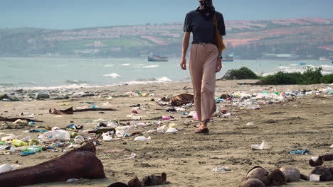 mujer con máscara caminando por la playa con basura y cáscaras de coco