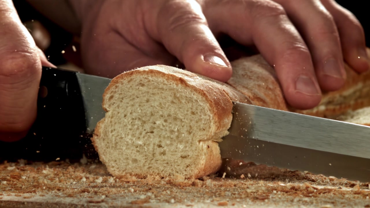 Primo piano di una mano che affetta una baguette fresca con un coltello al rallentatore