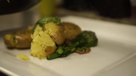 Close-Up---Putting-grilled-steamed-fresh,-green-broccoli,-spinach,-onion,-herbs-and-potatoes-on-a-white-plate