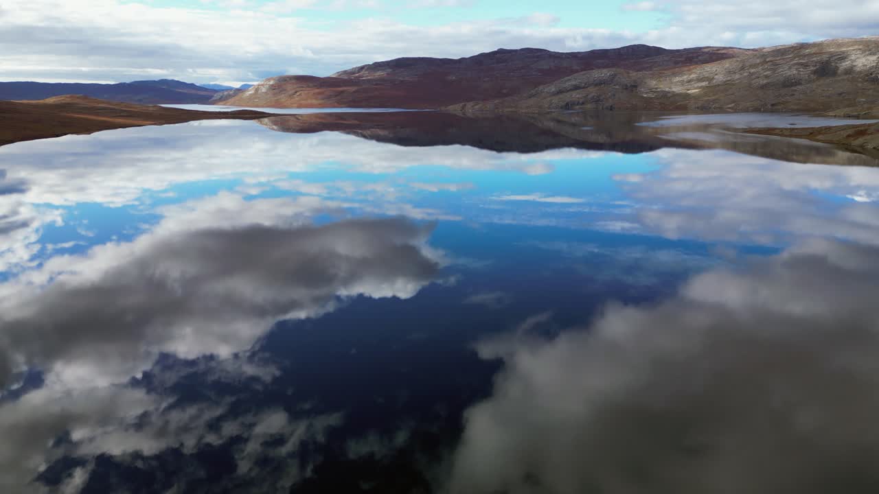 Tilt up from lake surface mirroring cloud sky to distant mountains