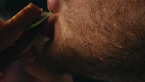 hombre hambriento comiendo sándwich en la sala de la noche de cerca. hombre disfrutando de una cena vegetariana