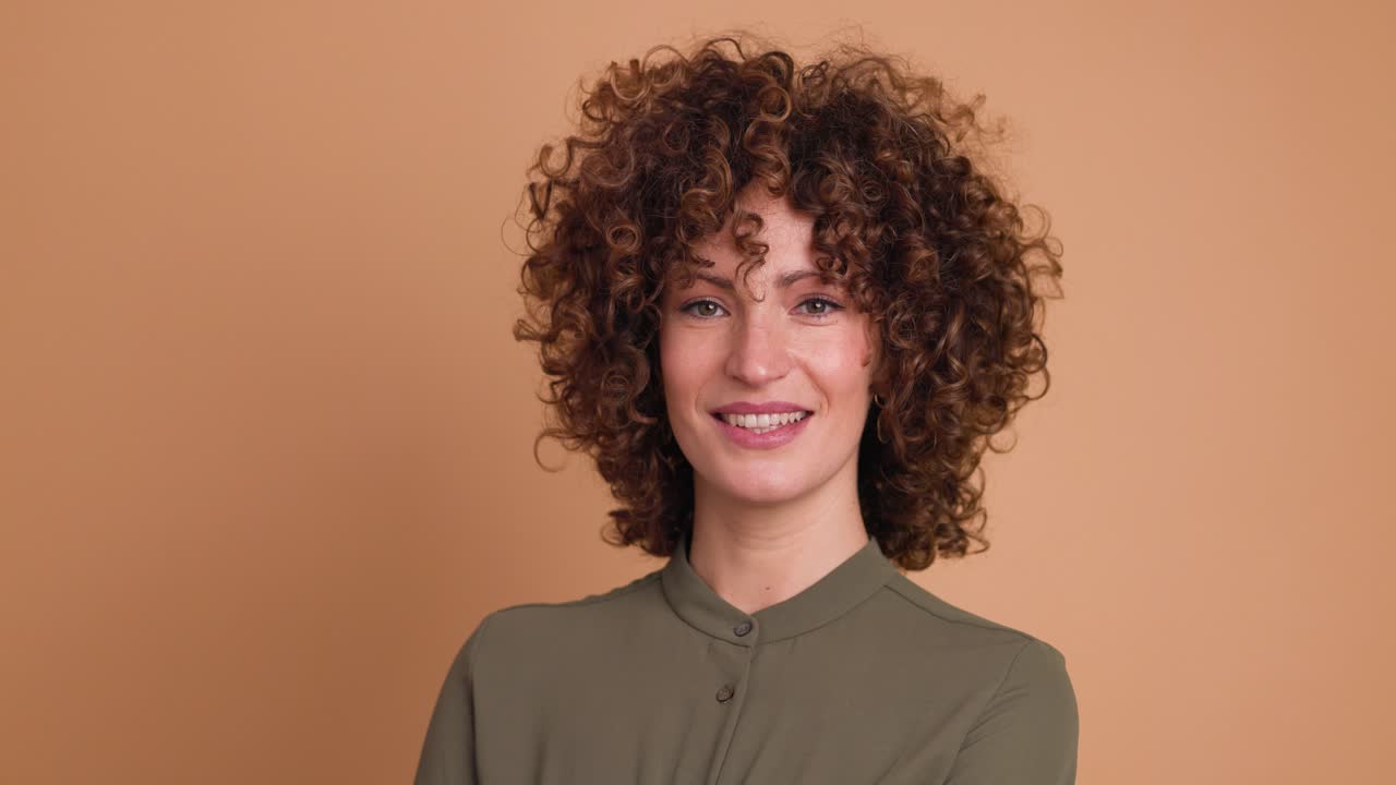 Smiling standing young curly haired woman on beige background