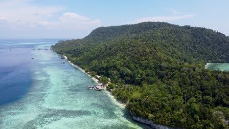 aerial drone view rising over white sandy beaches and remote waterfront huts on rainforest covered island in raja ampat, west papua, indonesia