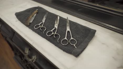 Scissors-And-Shaving-Tools-In-The-Towel,-With-A-Neck-Duster-Brush-On-Top-Of-The-Barber-Shop-Table